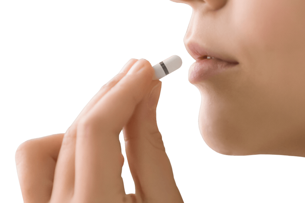 A person holding a small capsule-sized device near their lips, preparing to swallow it.