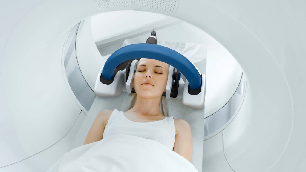 A patient with eyes closed in AiM Medical Robotics' MRI-compatible neurosurgical robot and MRI machine.