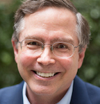 Man with glasses smiling outdoors.