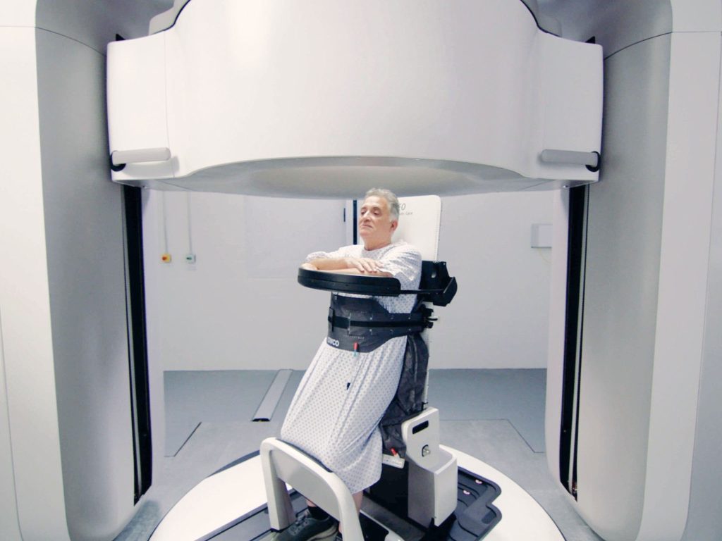 A patient sitting in Leo Cancer Care's upright medical imaging device. in a clinical setting.