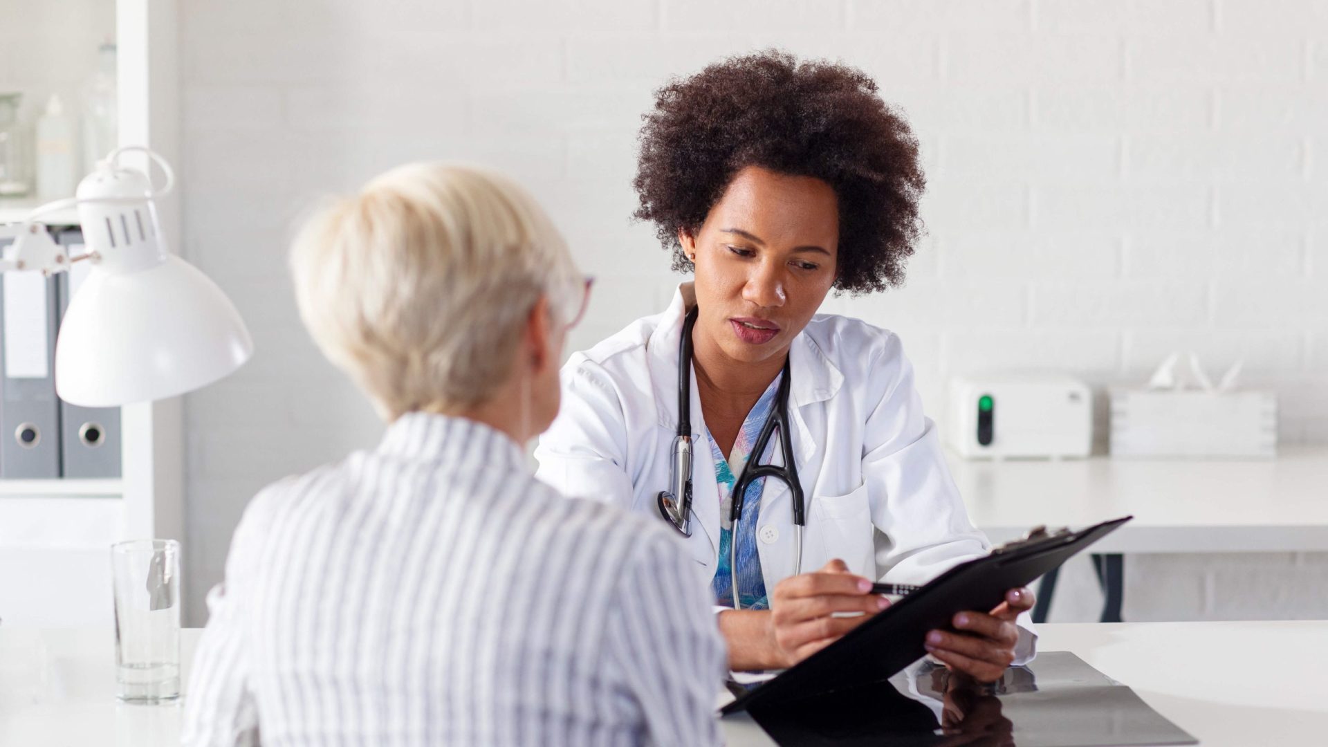 A female doctor discussing medical records with a patient in a clinic.