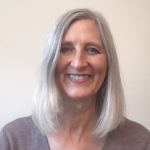 A smiling woman with shoulder-length gray hair against a neutral background.