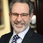 A smiling man with glasses wearing a suit and striped tie.