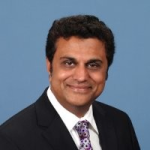 A professional headshot of a smiling man wearing a suit and tie.