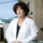 A woman in a lab coat standing outdoors near the water.