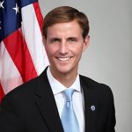 A man in a suit and tie standing in front of an american flag.