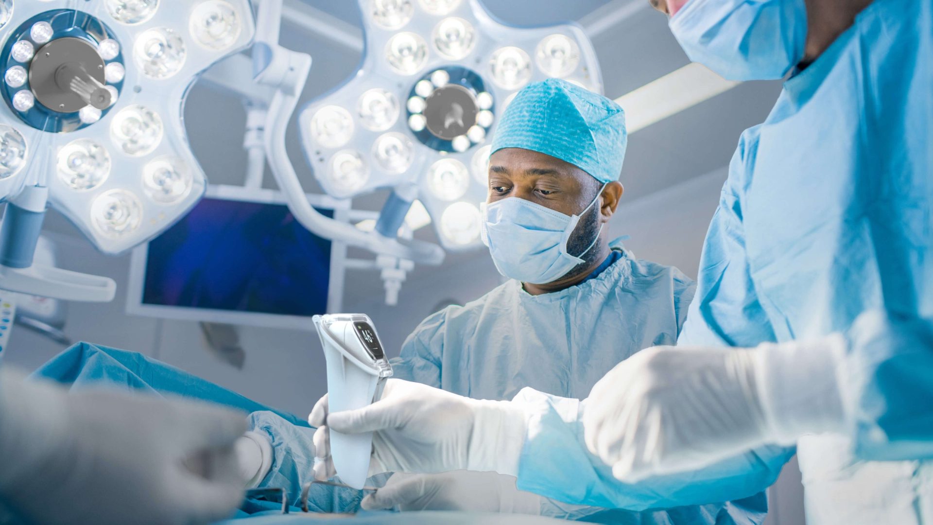 Surgeon viewing the screen of the ViOptix Intra.Ox handheld tissue oxygenation monitor during a surgical procedure in the operating room.