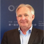 Man in a suit smiling at an event with a promotional banner in the background.