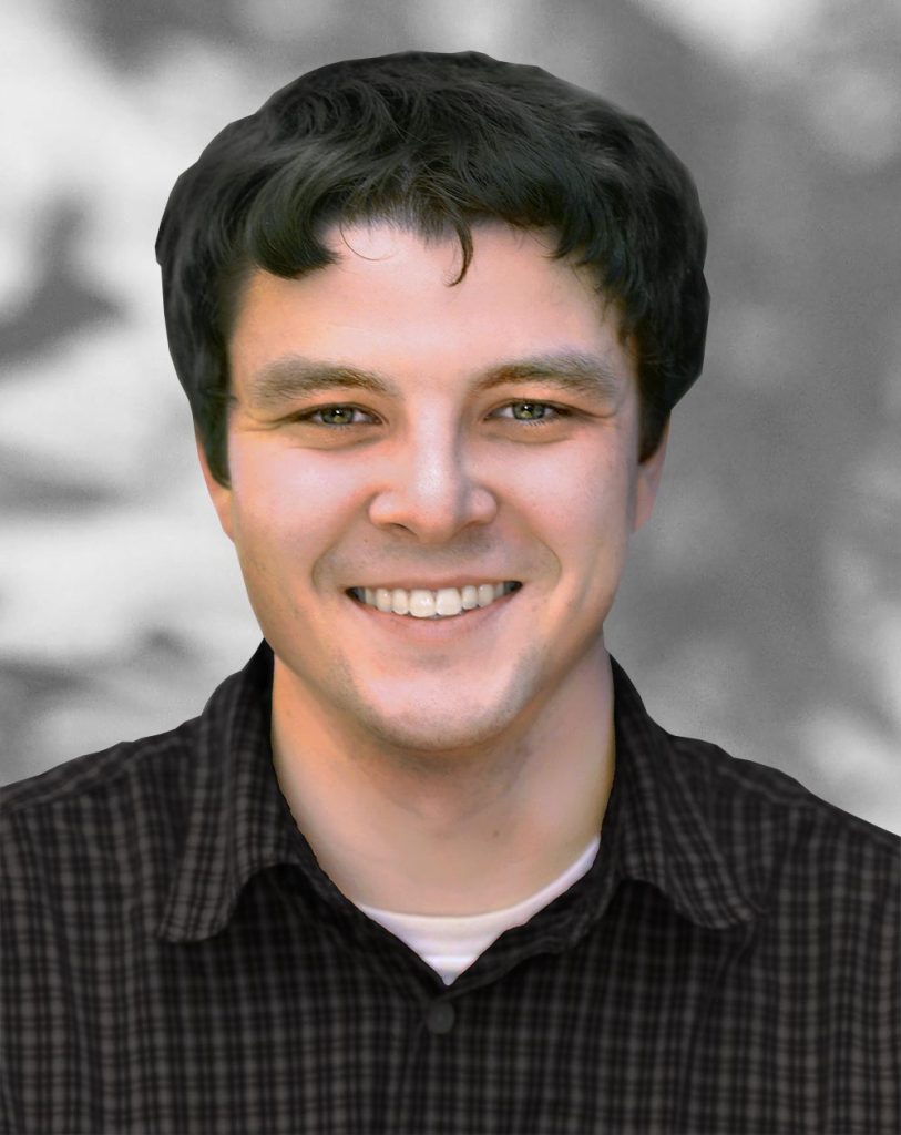 A portrait of Alex Margiott, a smiling man with dark hair wearing a checked shirt.