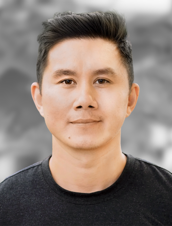 A portrait of Andrew Tran, a man with a modern hairstyle and black t-shirt standing against a gray background.