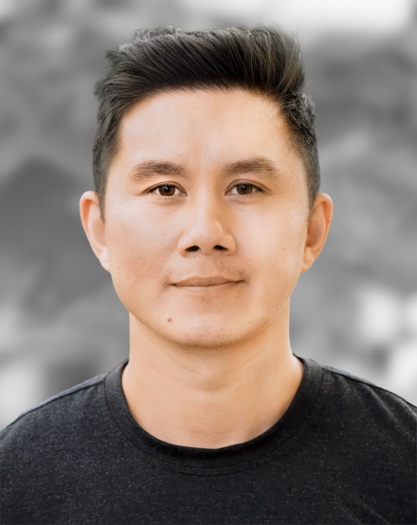 A portrait of Andrew Tran, a man with a modern hairstyle and black t-shirt standing against a gray background.