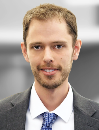 A portrait of Barry Wood, a smiling man with light stubble wearing a suit and tie.