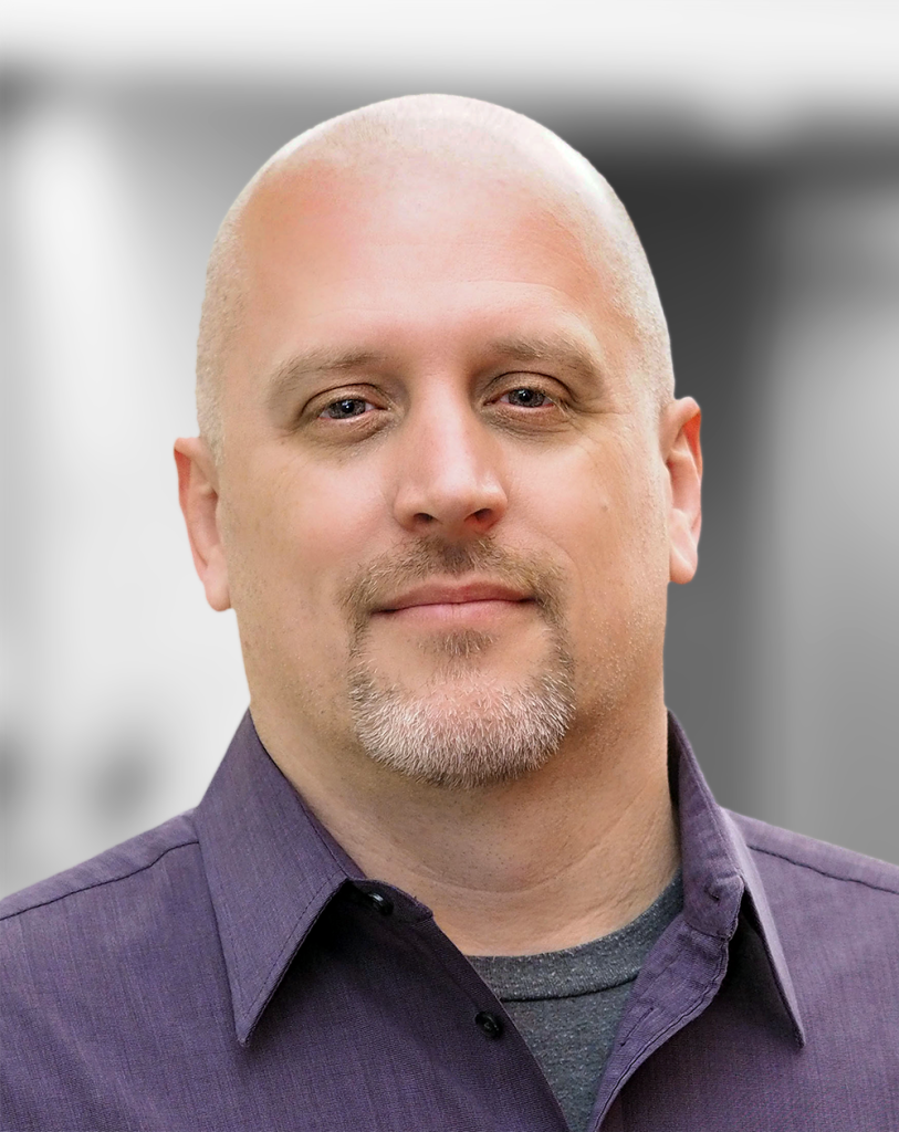 A portrait of Bob Mattson, a smiling man with a goatee, wearing a purple shirt, against a blurred background.