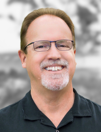 A portrait of Chris Storment, a man with glasses and goatee smiling.