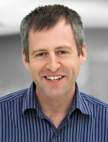 A portrait of Christopher Ellenor, a smiling man wearing a striped shirt.