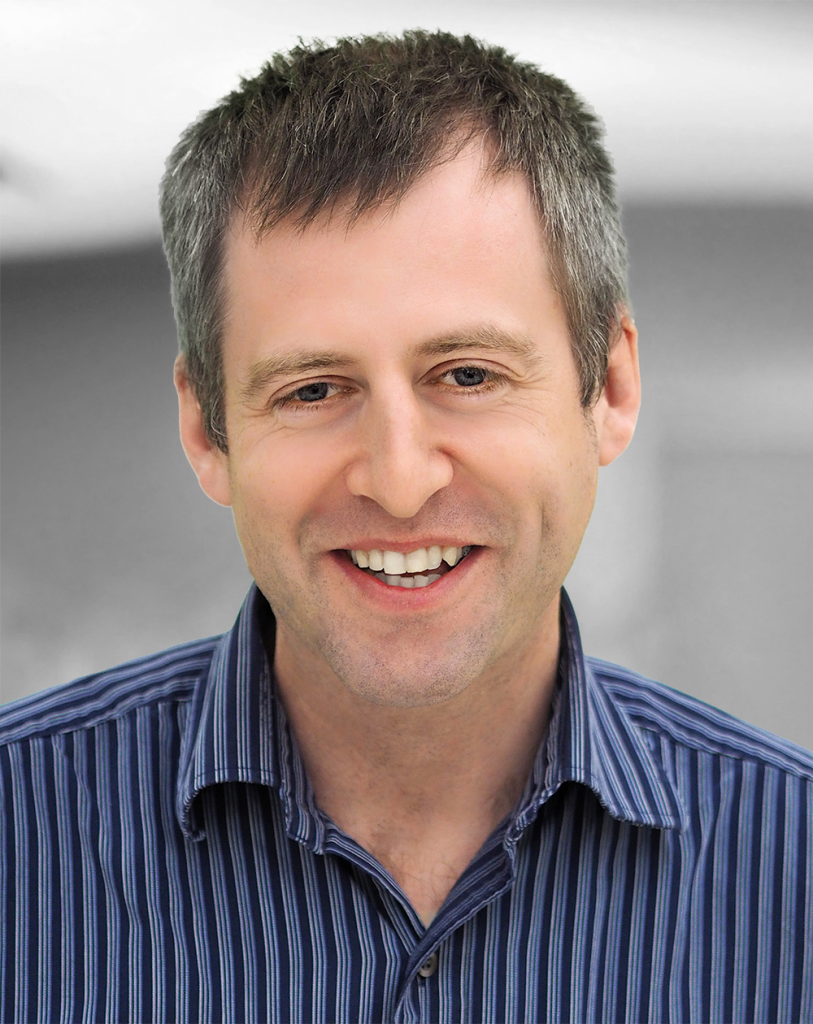 A portrait of Christopher Ellenor, a smiling man wearing a striped shirt.