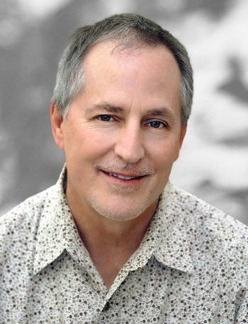 A portrait of Christopher Mitchell, a smiling man with gray hair wearing a patterned shirt.