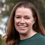 A portrait of Debbie Saunders, a smiling woman with long hair outdoors.