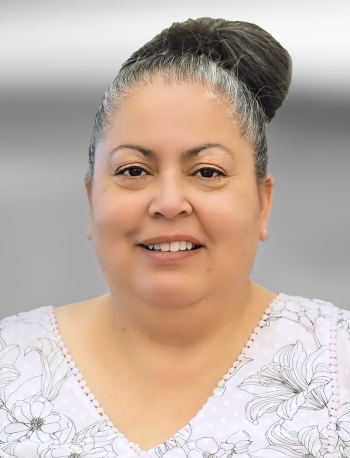 A portrait of Diana Satele, a woman with her hair in a bun, wearing a floral blouse, smiling at the camera.