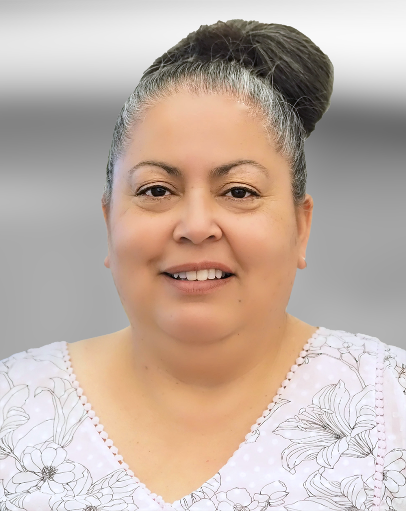 A portrait of Diana Satele, a woman with her hair in a bun, wearing a floral blouse, smiling at the camera.