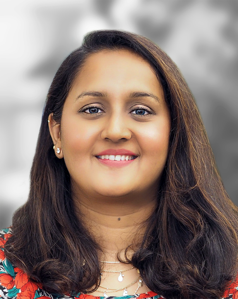 A portrait of Dickshitha Thyagharajon, a smiling woman with shoulder-length hair and a floral top against a blurred background.