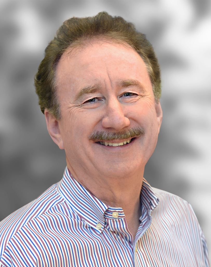 A portrait of Ed Solomon, a smiling man with a mustache wearing a striped shirt.