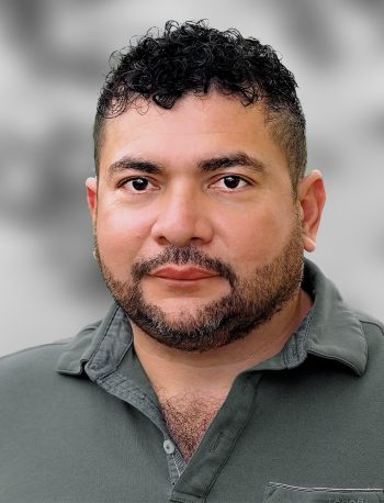 A portrait of Erick Guevara, a man with short curly hair and a beard wearing a polo shirt against a blurred background.