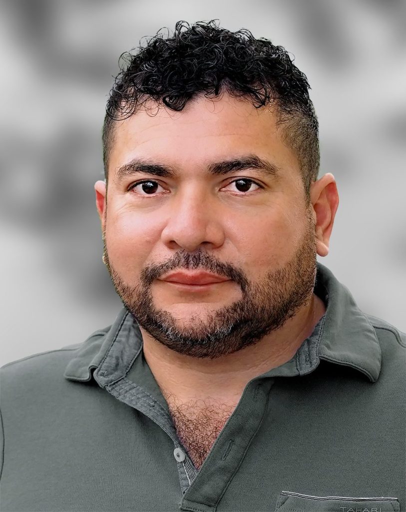 A portrait of Erick Guevara, a man with short curly hair and a beard wearing a polo shirt against a blurred background.