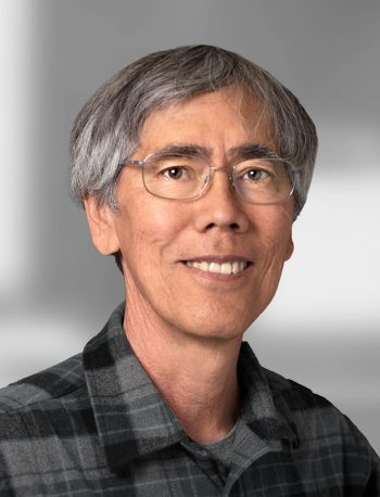 A portrait of Keith Nishihara, a smiling man with gray hair wearing glasses and a plaid shirt.