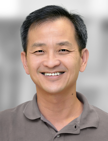 A portrait of Jamie Ku, a man smiling at the camera against a gray background.