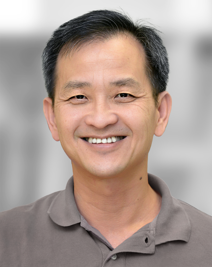 A portrait of Jamie Ku, a man smiling at the camera against a gray background.