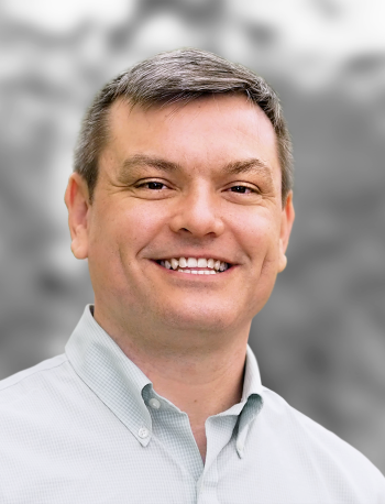 A portrait of Jeffrey Perkins, a smiling man in a buttoned shirt with a gray background.