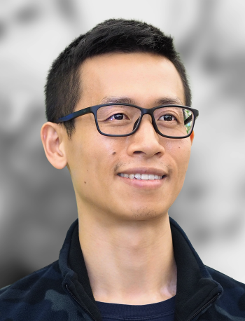 A portrait of Ji Wang, a smiling man wearing glasses with a gray background.