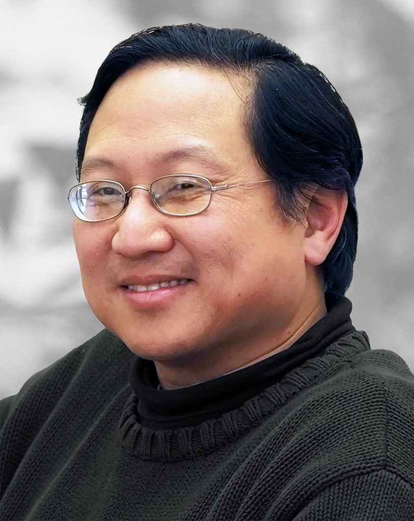 A portrait of Joe Lin, a smiling man with glasses wearing a black sweater.