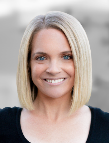 A portrait of Kelly Martin, a smiling woman with shoulder-length blonde hair and blue eyes against a blurred background.