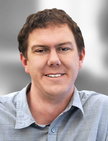 A portrait of Kevin Dunk, a smiling man with short brown hair wearing a collared, button-up shirt.