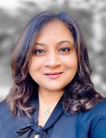 A portrait of Pooja Kartik, a woman with shoulder-length hair, wearing a black top with a bow at the collar.