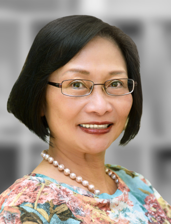 A portrait of Quan Tran, a smiling woman with short hair wearing glasses, a floral blouse, and a pearl necklace.