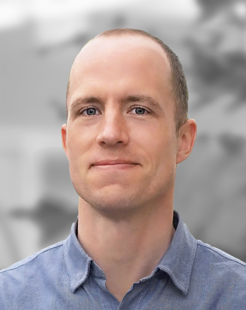 A portrait of Robert de Saint Phalle, a smiling man wearing a blue shirt, with a blurred background.