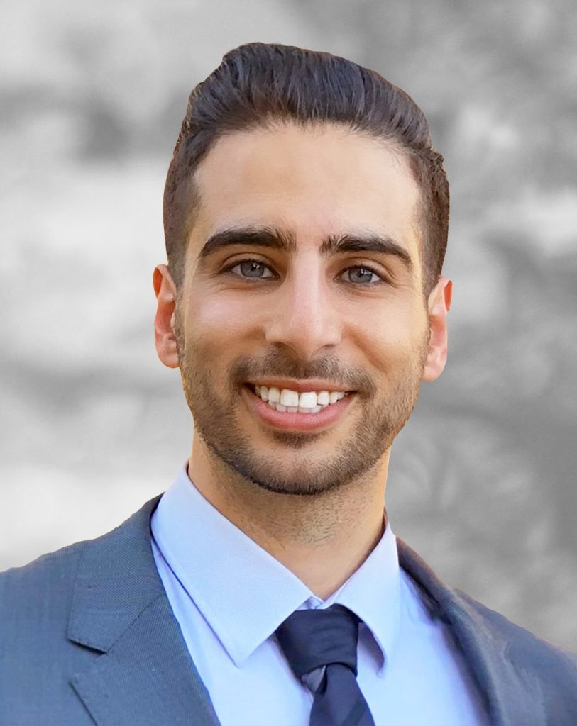 A portrait of Shehadeh Dajani, a smiling man wearing a suit and tie against a blurred background.