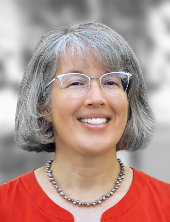 A portrait of Sheila Hemami, a smiling woman with gray hair wearing glasses and a red blouse against a gray background.