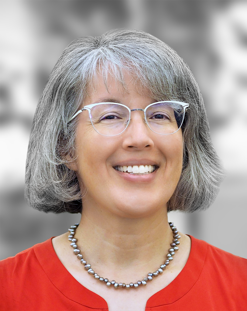 A portrait of Sheila Hemami, a smiling woman with gray hair wearing glasses and a red blouse against a gray background.