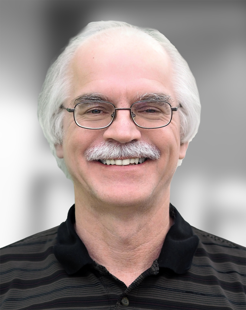 A portrait of Steven Kuhn, a smiling man with a white mustache and glasses against a gray background.