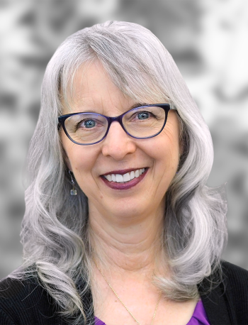 A portrait of Theresa Christian, a smiling woman with gray hair and glasses, wearing a purple top and earrings against a blurred grayscale background.