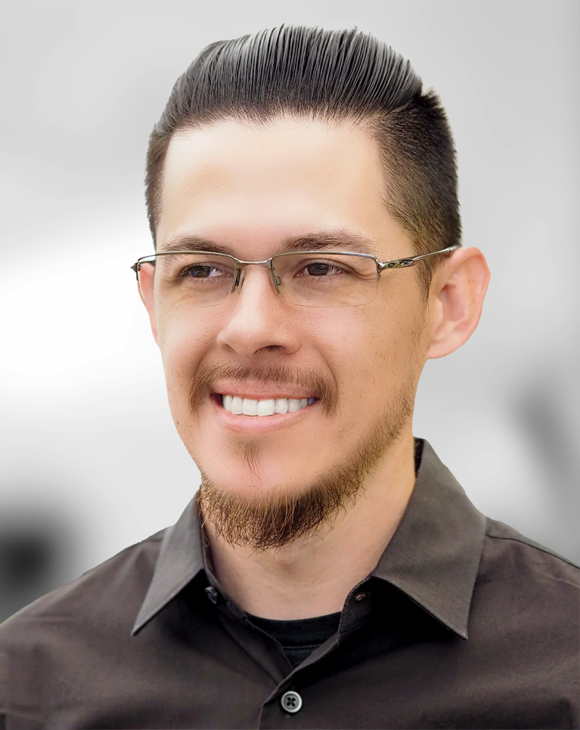 A portrait of Thomas Nocon, a smiling man with glasses and a combed-back hairstyle.