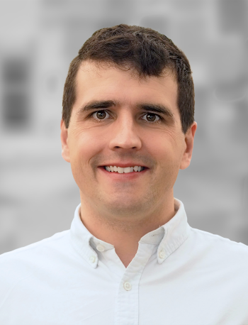 A portrait of Tim Sauder, a man with dark hair and a white shirt smiling against a blurred background.