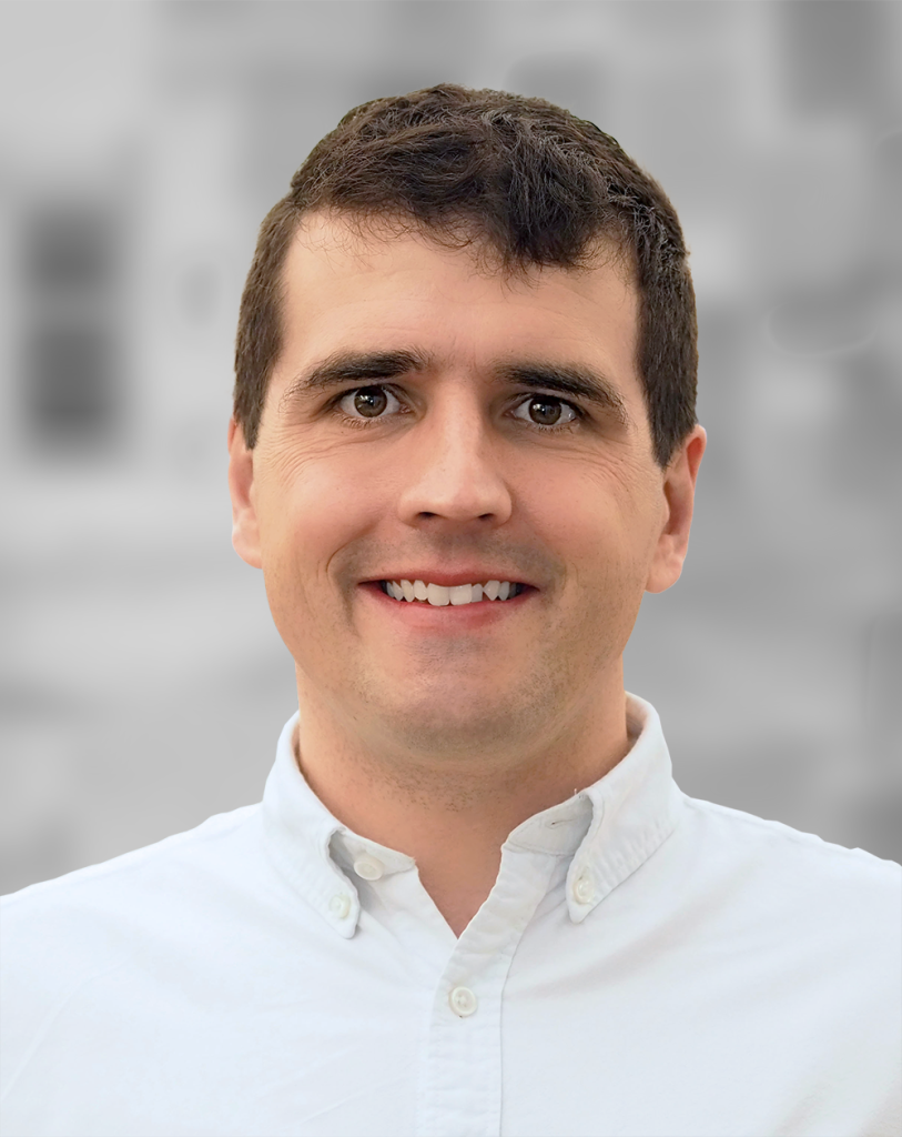 A portrait of Tim Sauder, a man with dark hair and a white shirt smiling against a blurred background.