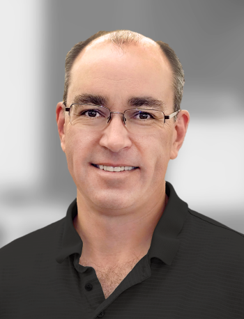 A portrait of Todd Harris, a man with glasses wearing a black shirt against a grey background.
