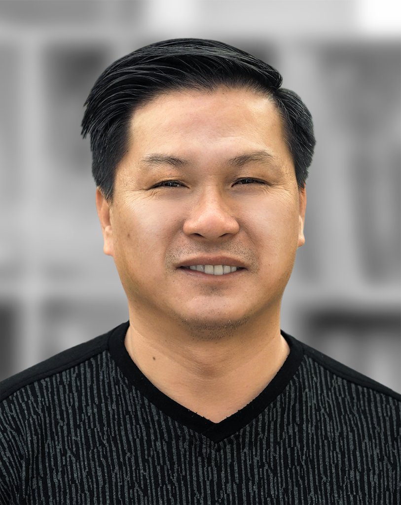 A portrait of Ty Ta, a man wearing a black shirt smiling against a blurred gray background.