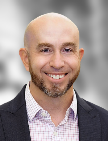 A portrait of Vrad Levering, a smiling man with a beard and plaid shirt smiling against a blurred background.